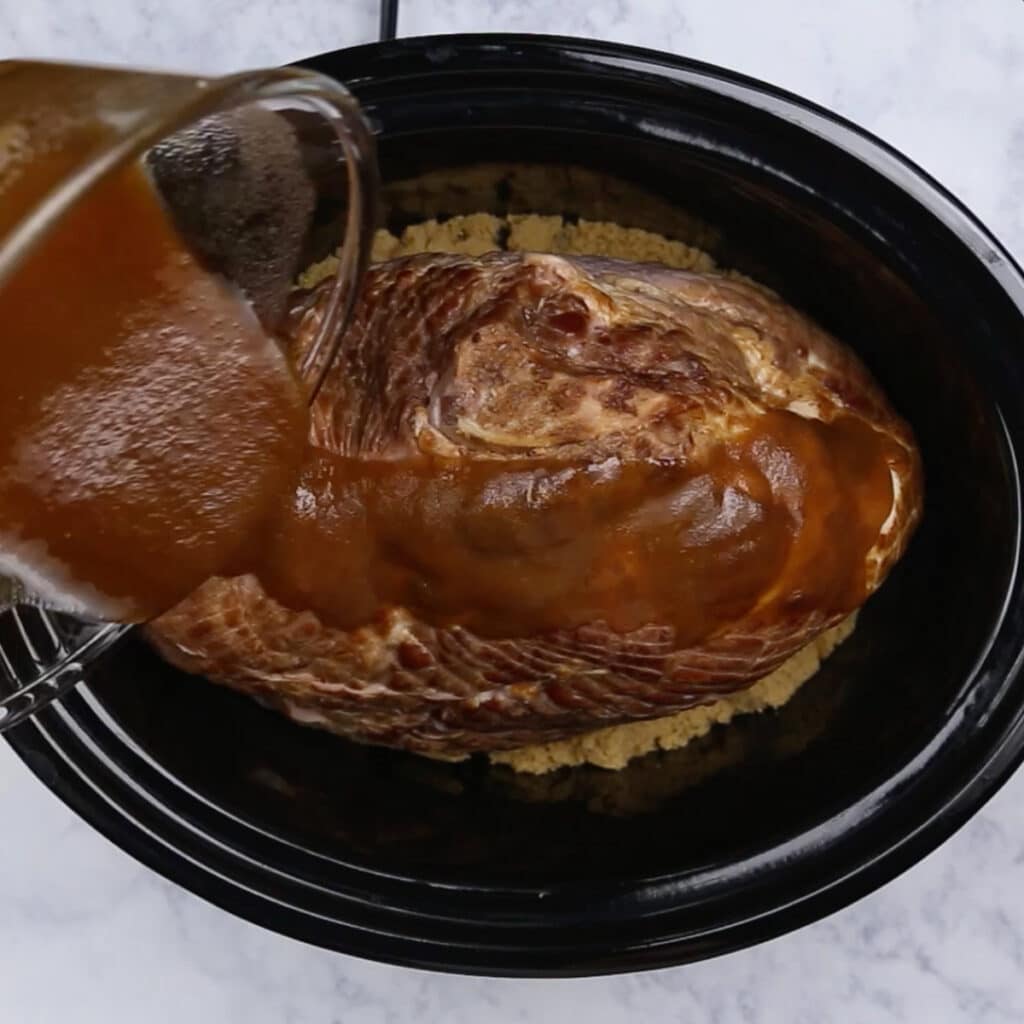 Sauce being poured on a spiral ham in a crockpot.