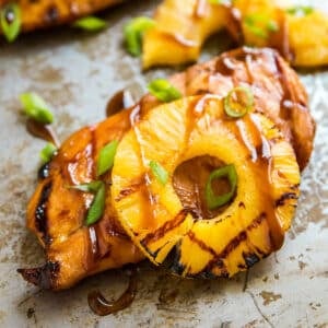 A piece of pineapple chicken breast with a grilled pineapple slice on a pan with other pieces behind it.