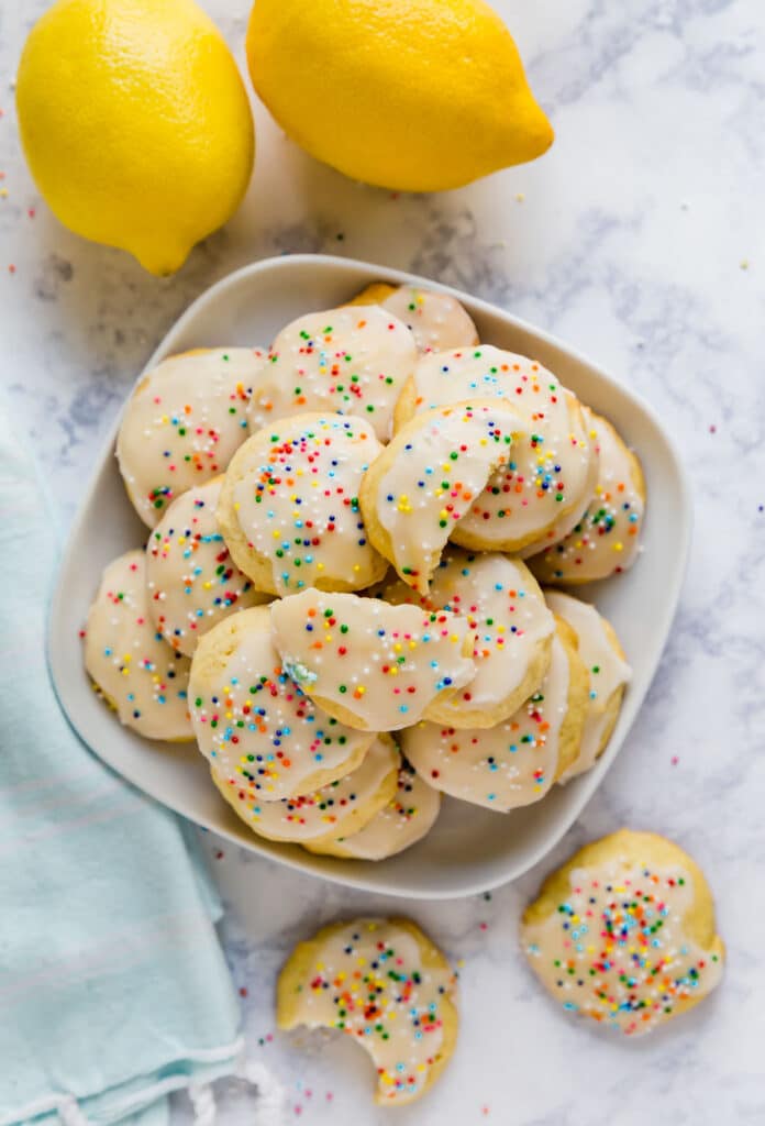 An overhead image of a platter of sour cream cookies with lemons and a light blue towel next to it.