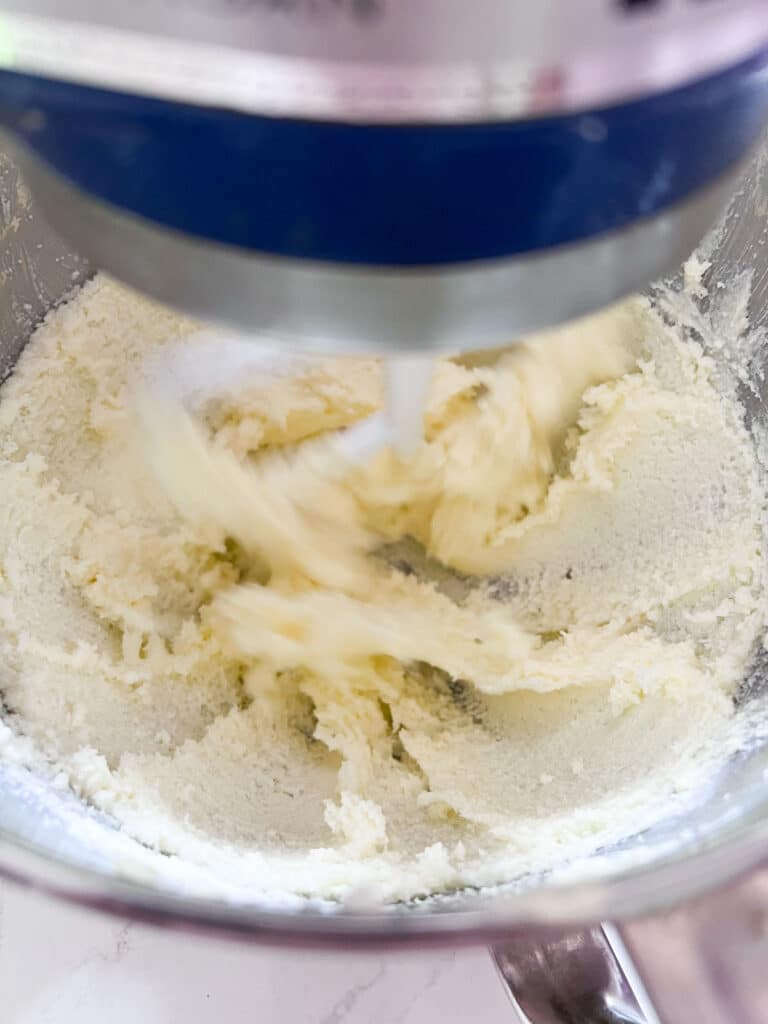 Butter and sugar being mixed in a blue stand mixer.