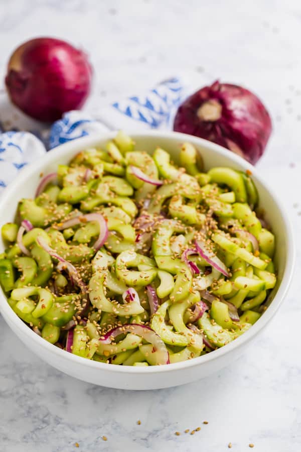 A bowl of cucumber salad with onion behind it.