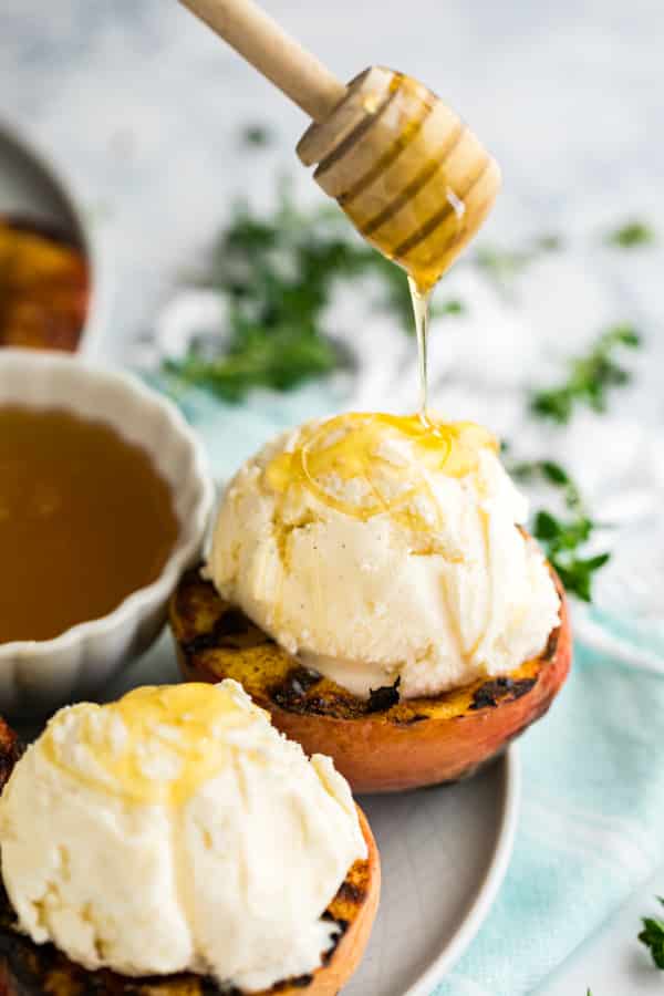 Honey being drizzled over the ice cream on a grilled peach