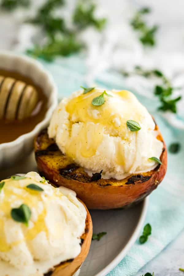 Grilled peaches on a plate with ice cream on top.