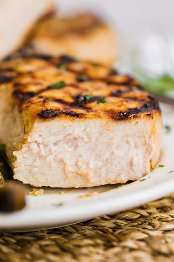 A straight on image of a grilled pork chop with a piece cut off revealing the perfectly cooked inside.