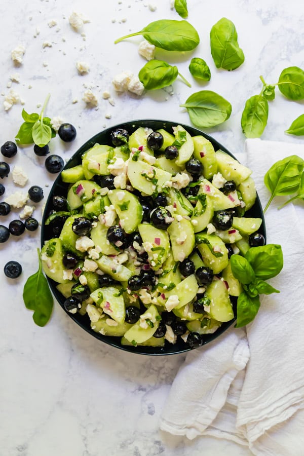 An overhead image of a bowl of cucumber salad recipe with feta and blueberries