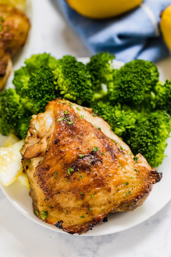 A chicken thigh on a plate with broccoli.
