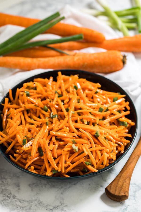 A bowl of carrot salad with carrots behind it.