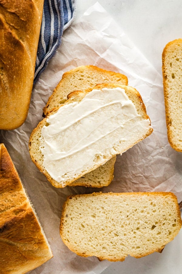 An overhead image of a stack of slices of sandwich bread with butter on the top slice.