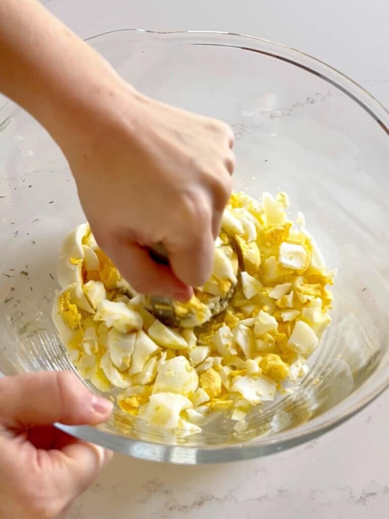 A hand cutting hard boiled eggs in a glass bowl.