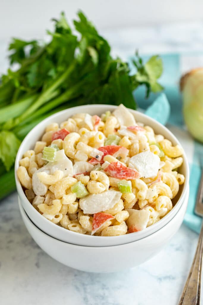 A bowls of mac salad with crab with celery in the background.