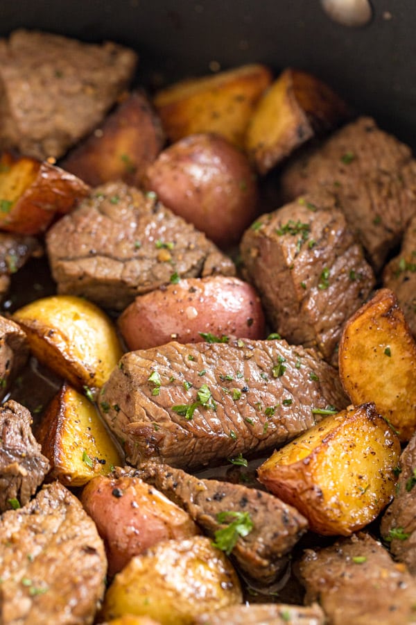 A close up shot of steak and potatoes in a pan, focusing on a chunk of steak.