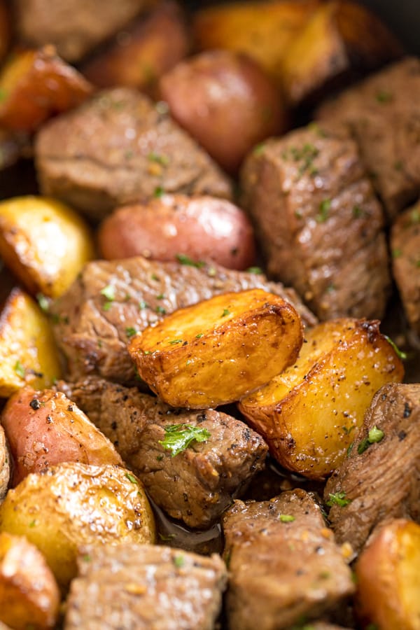 A close up shot of a potato in a pan with steak and potatoes around it.