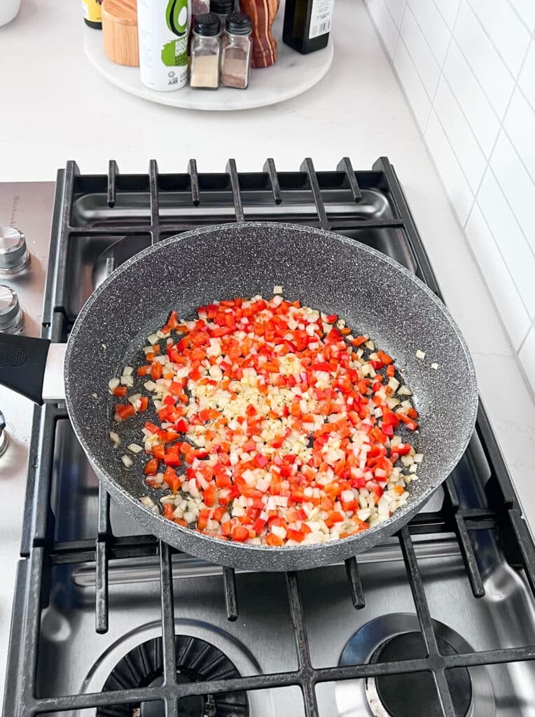 Onions, peppers and garlic in a skillet sautéing on a stove.