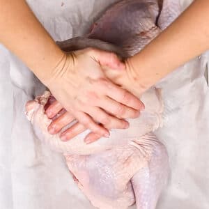 An overhead image of two hands pushing down on the turkey breasts to flatten the bird.