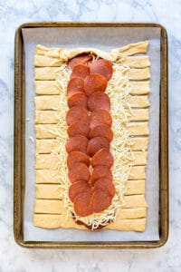 Raw pizza braid that shasnt been braided on a parchment lined sheet pan.