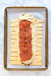 A raw pizza braid on a parchment lined sheet pan with the first couple of dough strips braided.