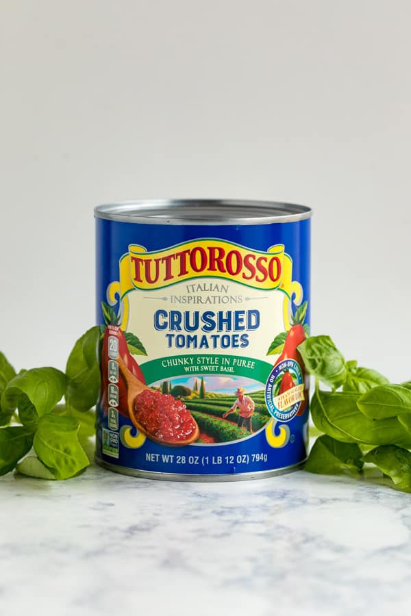A large can of Tuttorosso crushed tomatoes surrounded by fresh basil.