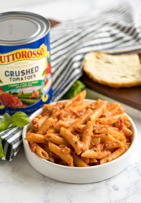 A plate of penne alla vodka with bread and a can of crushed tomatoes behind it.