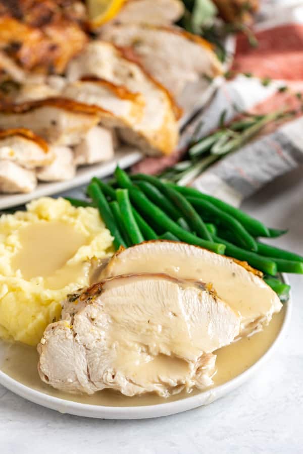 Sliced turkey breast on a plate with gravy, mashed potatoes and green beans.