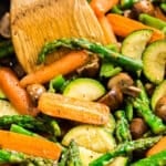 A close up image of sautéed veggies in a pan with a wooden turner in it.