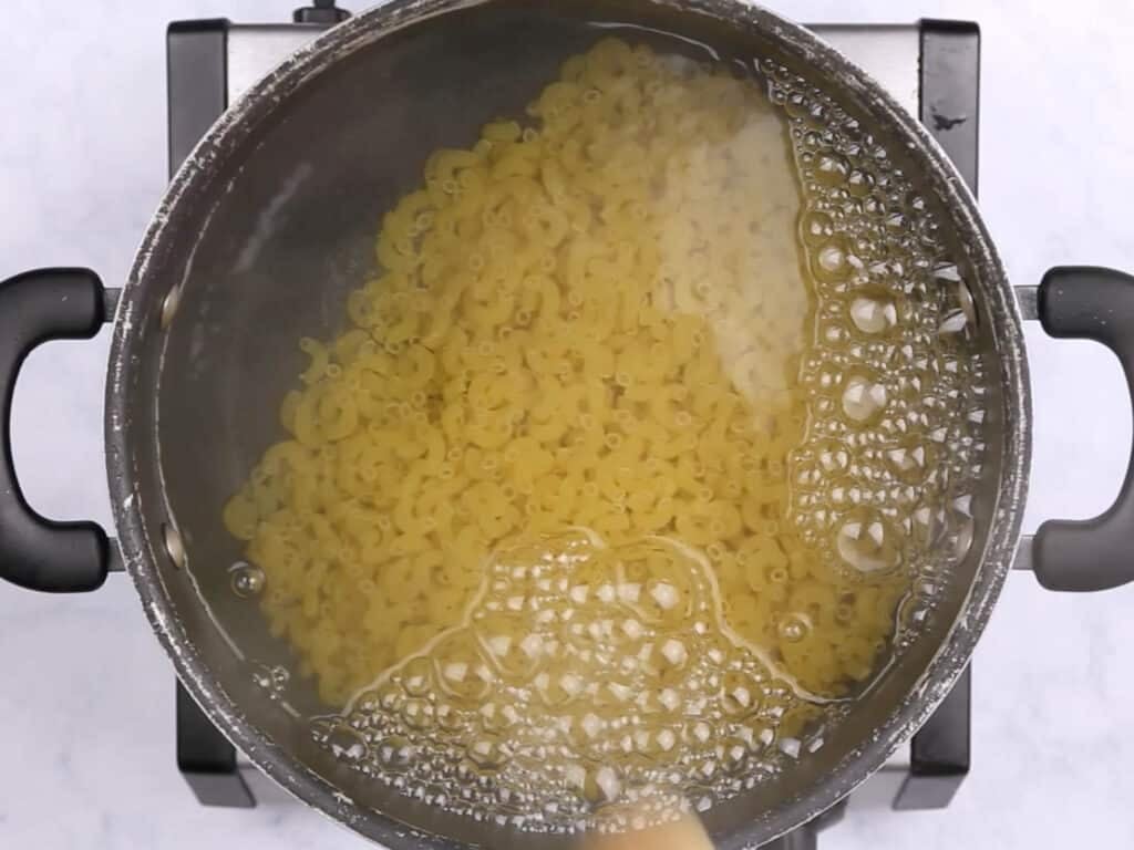 A pot of boiling water with elbow pasta in it.