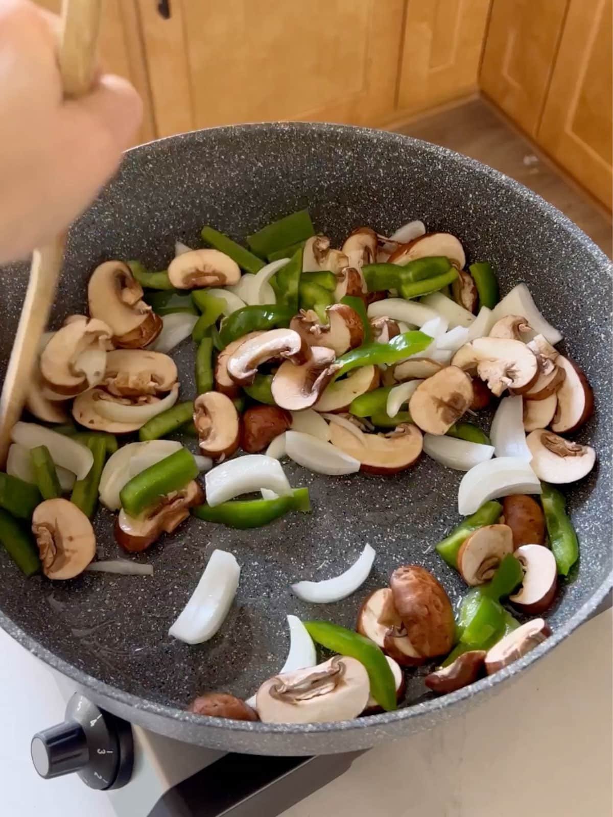 Onions, peppers and mushrooms in a skillet being sautéed.