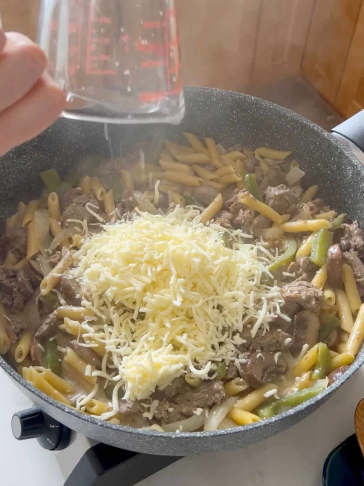 Shredded cheese added to skillet of pasta.
