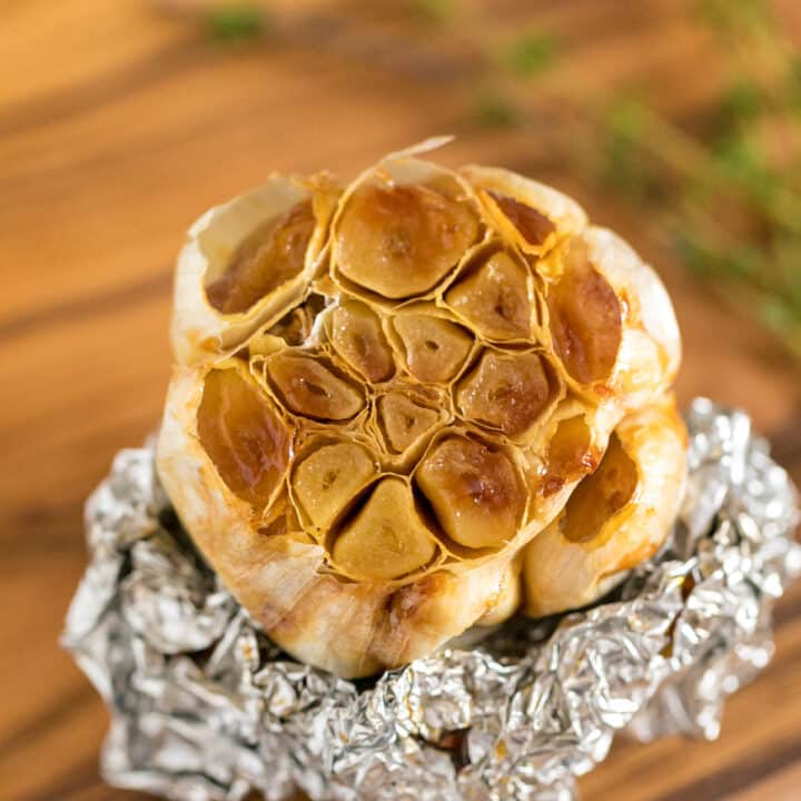 A close up image of a bulb of roasted garlic revealing it inside on top of some tin foil on a cutting board.