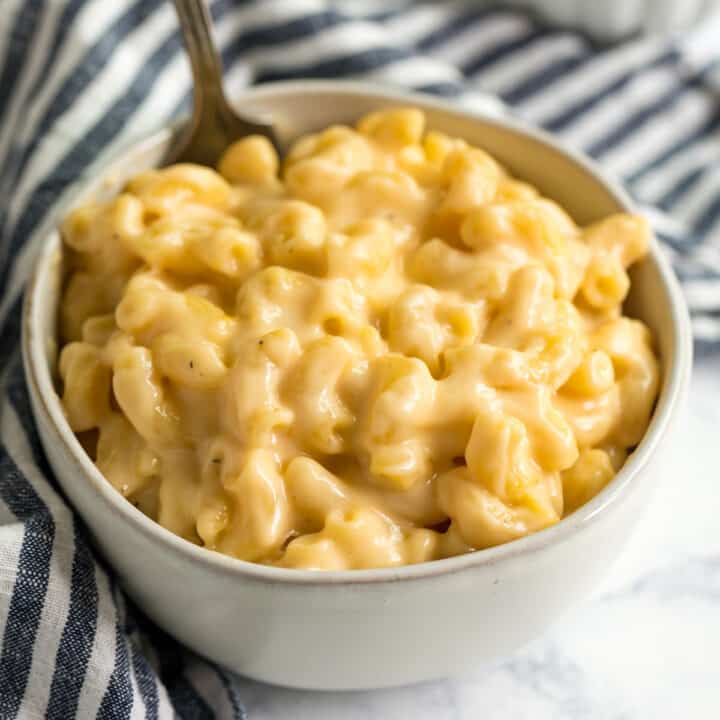 A square image of a bowl of creamy mac and cheese with a striped naplin and shredded cheese behind it.