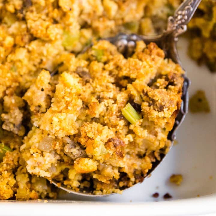 A close up of a serving spoon in a pan of dressing with some cornbread dressing on it.
