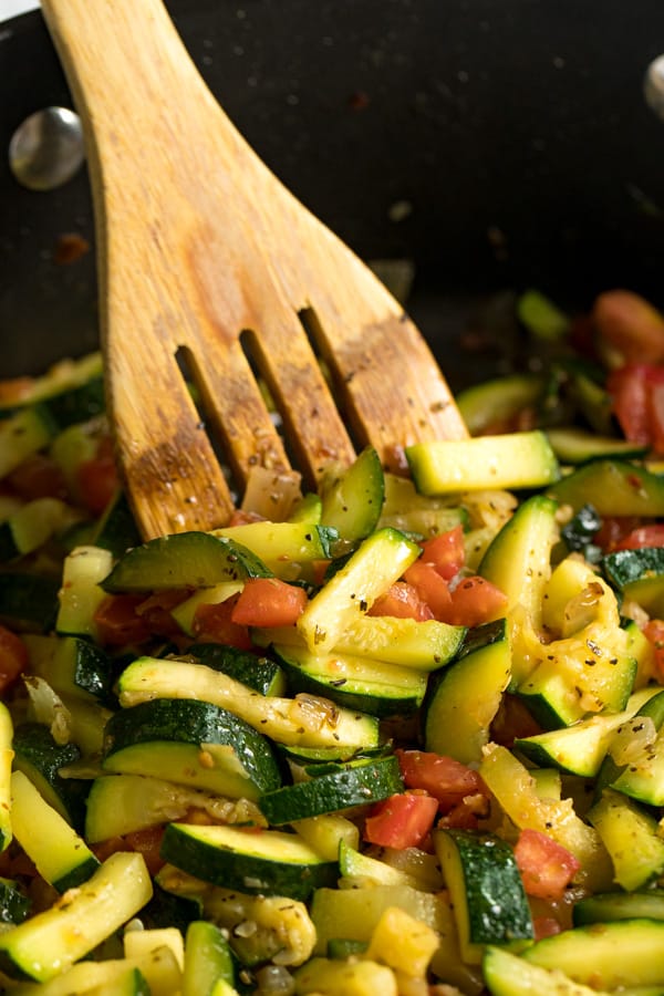 Sautéed Zucchini and Tomatoes in a sauté pan with a wooden spoon in it.