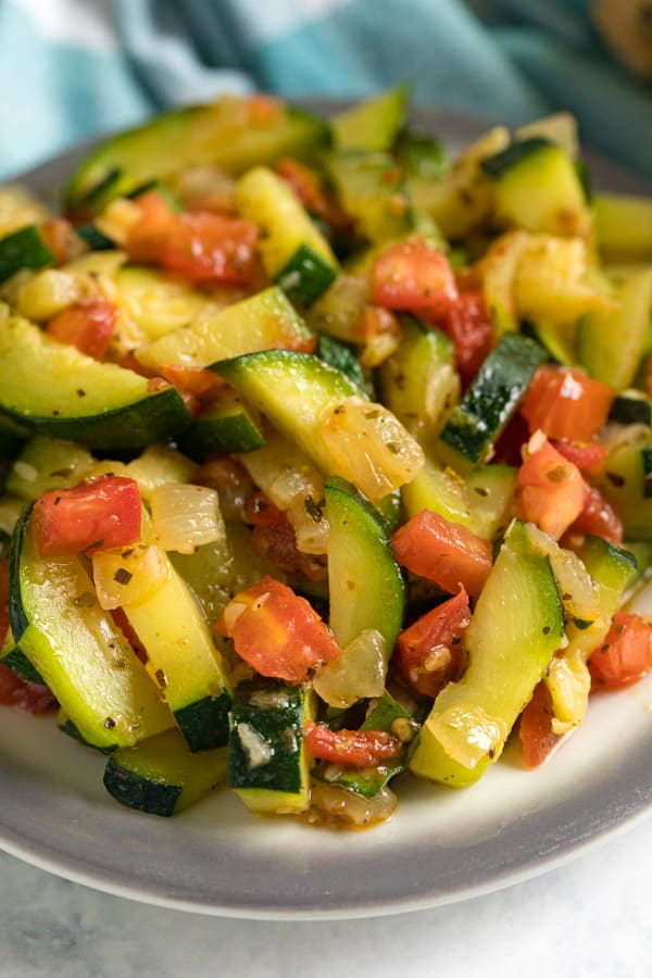 A close up of Sautéed Zucchini and Tomatoes on a grey rimmed plate.