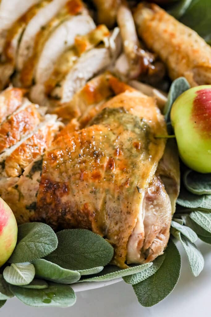A close up shot of a turkey thigh on a platter with sage and apples.