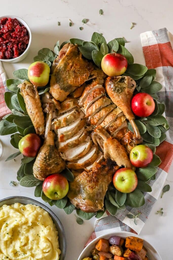 An overhead image of a carved up turkey on a platter with sage and apples.