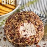 A cheese ball with some pulled off the front exposing the creamy inside of it with crackers and a striped napkin behind it.