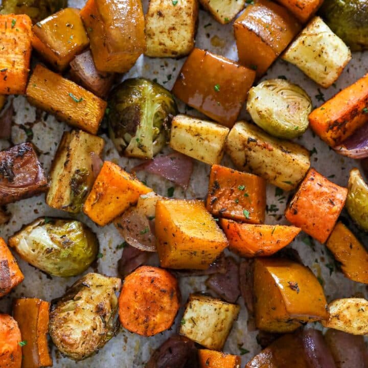 A close up overhead image of roasted root vegetables focusing on squash, carrots, parsnips, onion and Brussels sprouts.