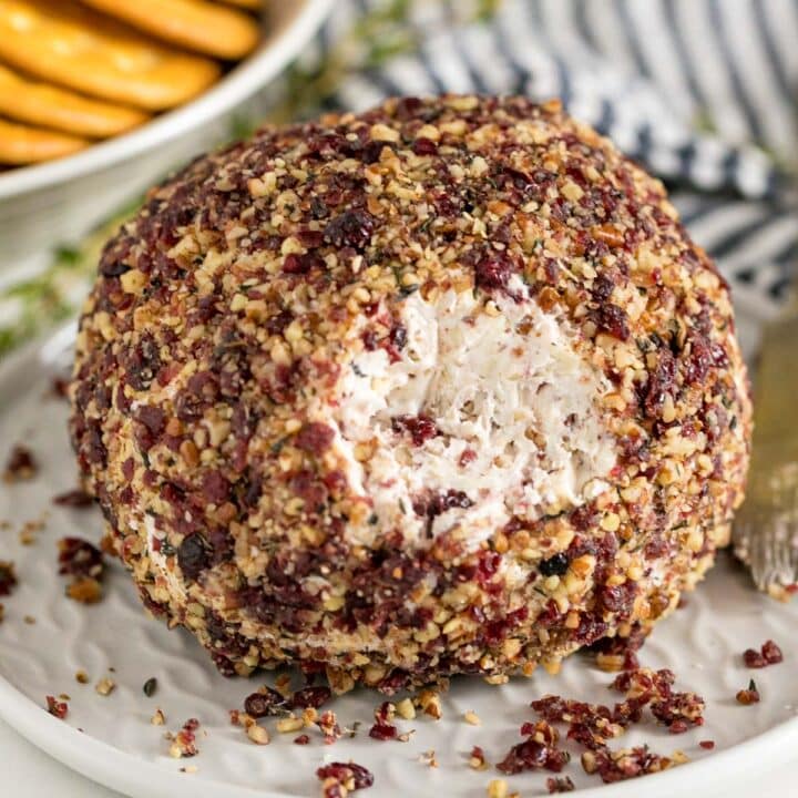 A cheese ball with some pulled off the front exposing the creamy inside of it with crackers and a striped napkin behind it.