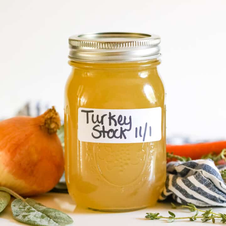 A straight-on shot of a closed jar of turkey stock with a label on the front and veggies and a napkin around it.
