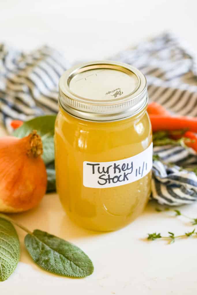 An angle shot of a closed jar of turkey stock with a label on the front and veggies and a napkin around it.