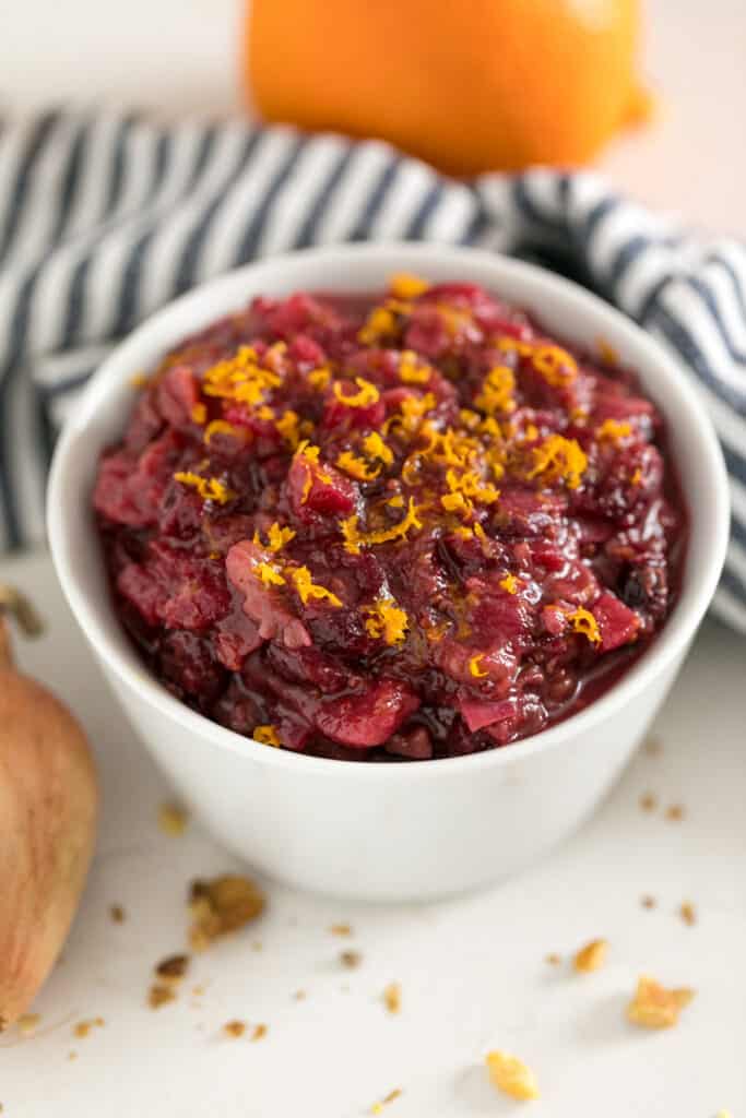 A close up image of a spoon lifting a scoop of this cranberry chutney recipe out of a white bowl full of it.