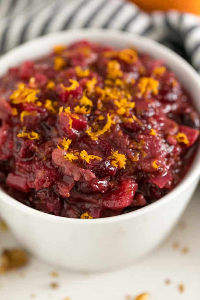 A close up image of Cranberry Chutney in a white bowl with orange zest on tops and a striped napkin in the background.