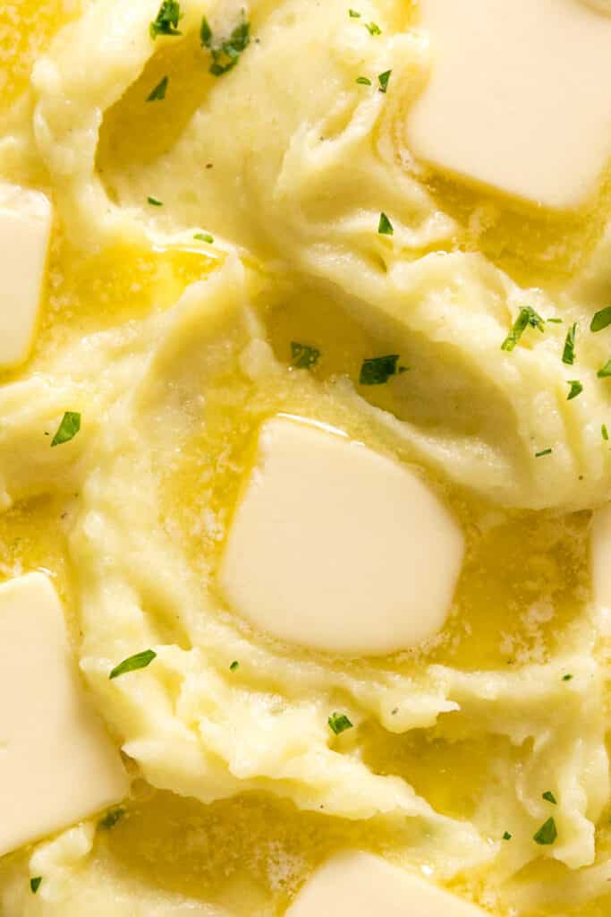 An overhead close up of the top of a bowl of this garlic mashed potatoes recipe with chopped parsley and melting butter pats on top of it.