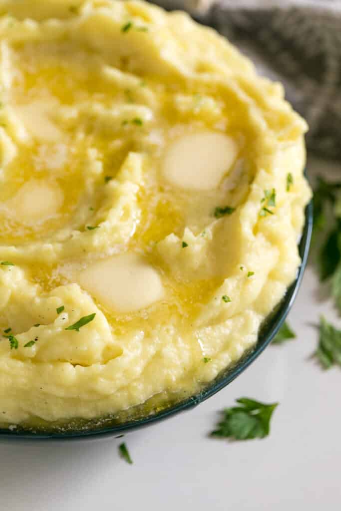The side of a bowl of mashed potatoes with melting butter pats on top of it in a blue bowl.