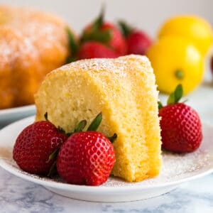 A slice of lemon poundcake on a white plate with strawberries next to it.
