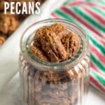 A glass jar of candied pecans with the pan and a green and red towel in the background.