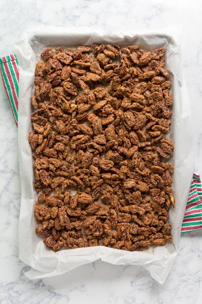 An overhead image of a parchment-lined pan of candied pecans on a red and green towel.