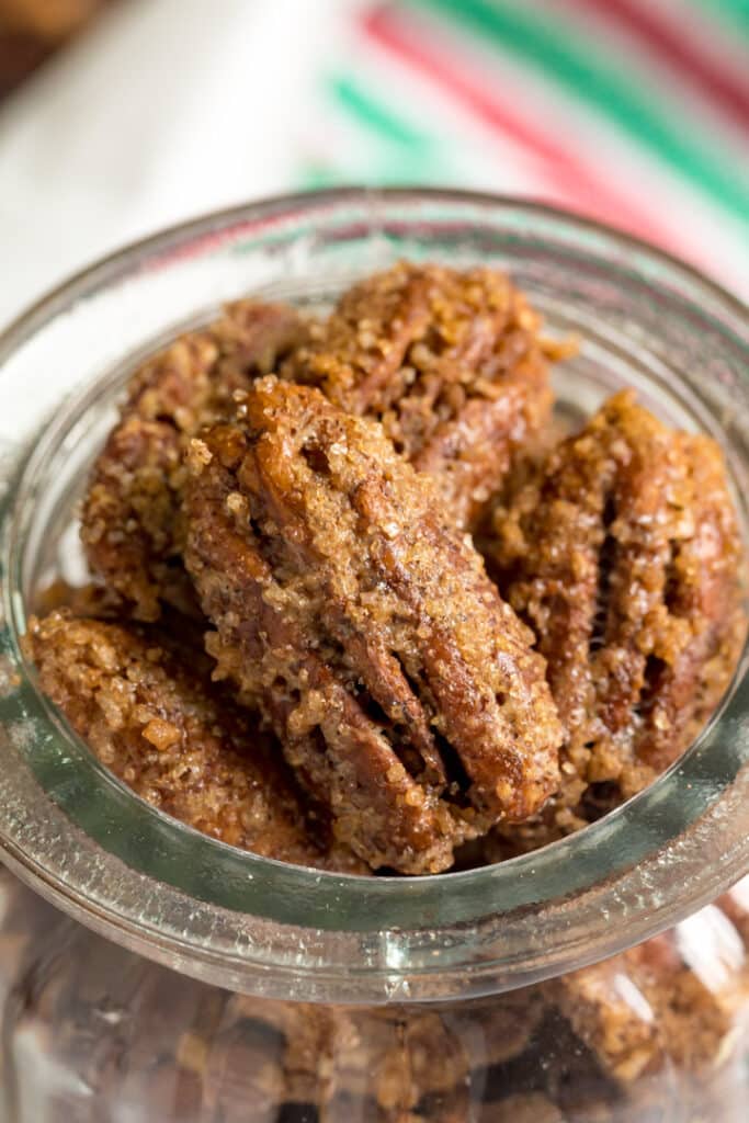 A close up image of the top of a glass jar containing candied pecans focusing on the pecan that's on top.