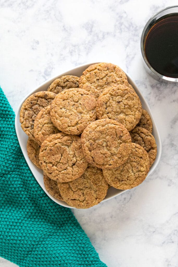 An overhead image of a square plate of snickerdoodle cookies next to a green towel and a cup of coffee.