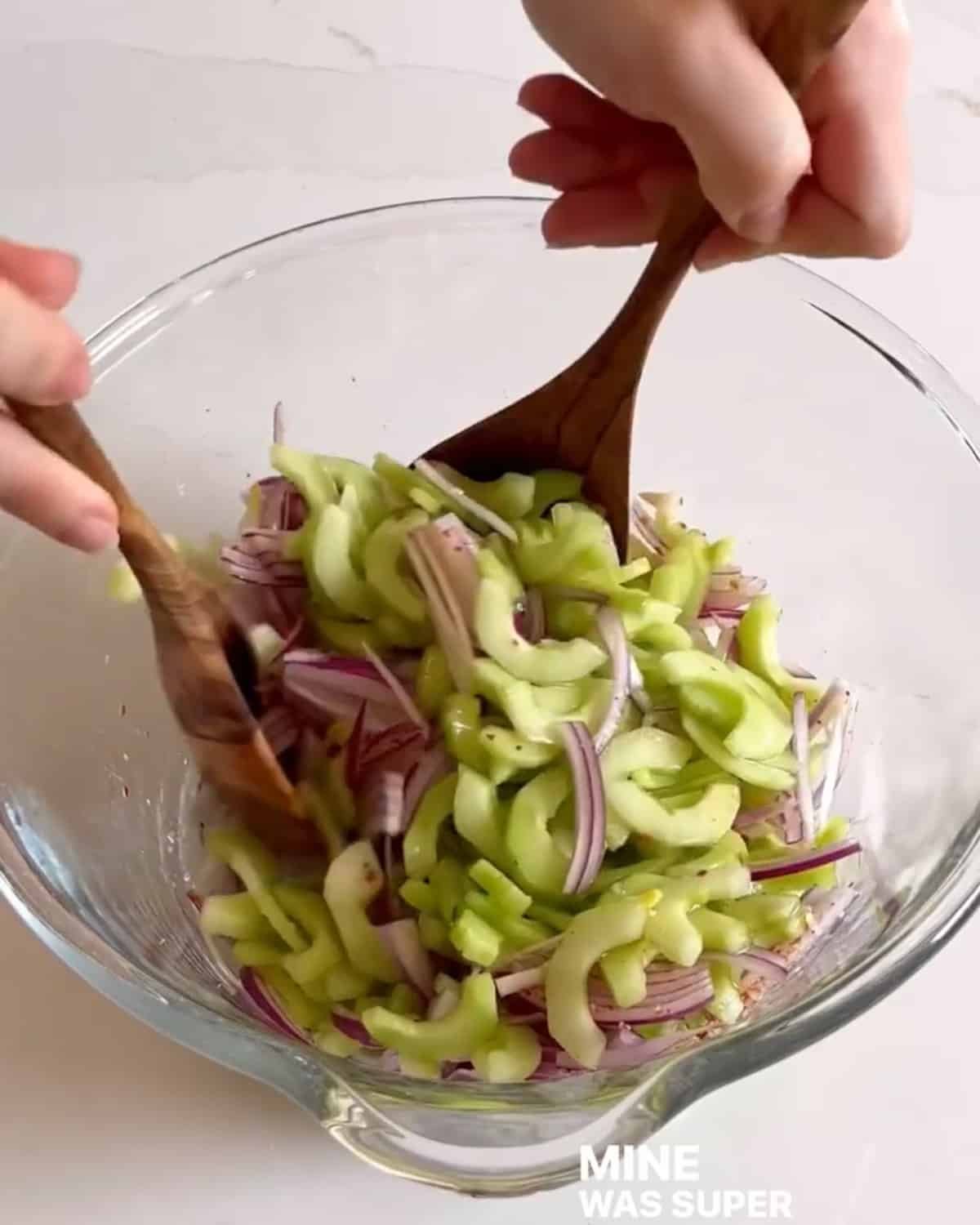Salad utensils tossing cucumber salad ingredients in a mixing bowl