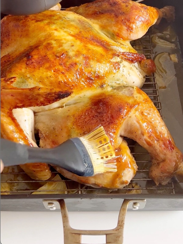 A hand brushing glaze onto a turkey.